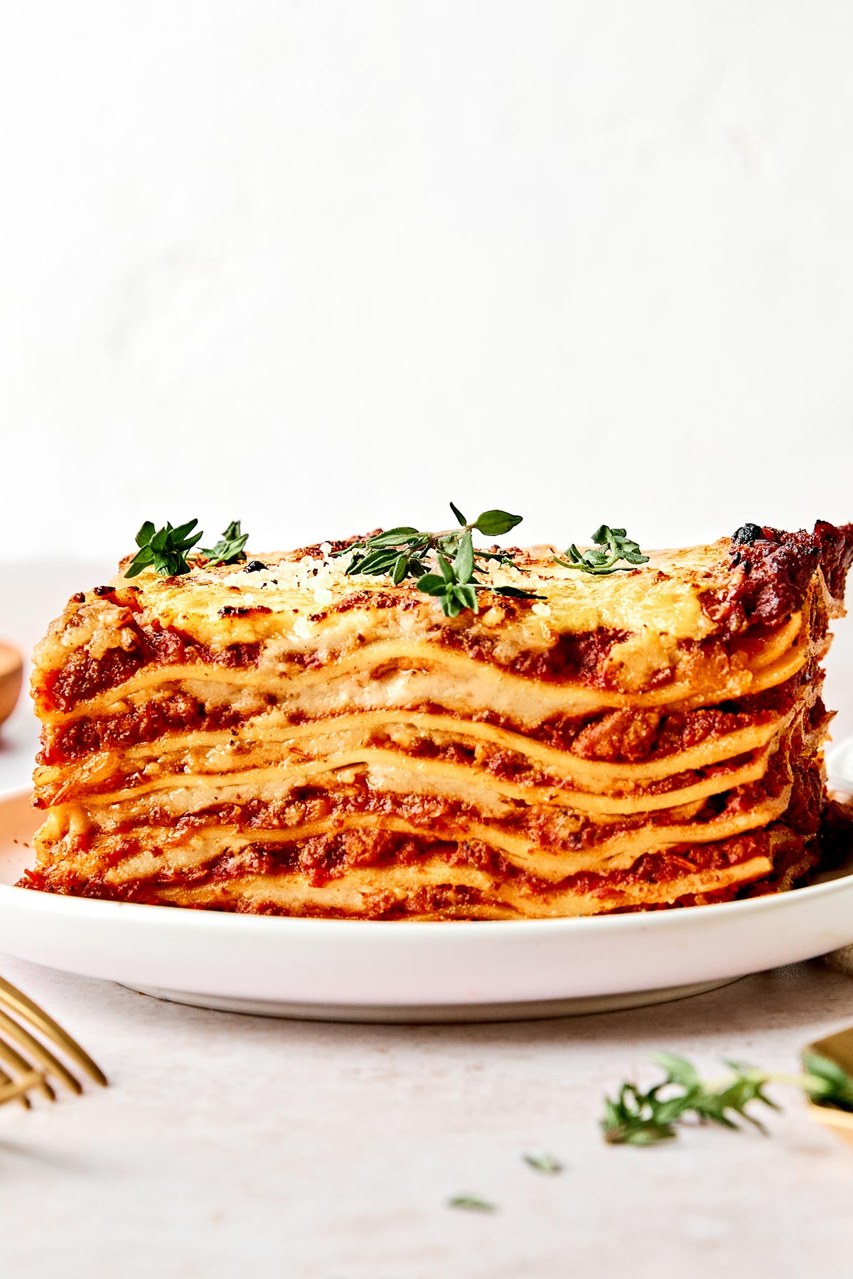 A close-up of a thick slice of lasagna with layers of pasta, tomato sauce, and melted cheese, garnished with fresh herbs, served on a white plate.