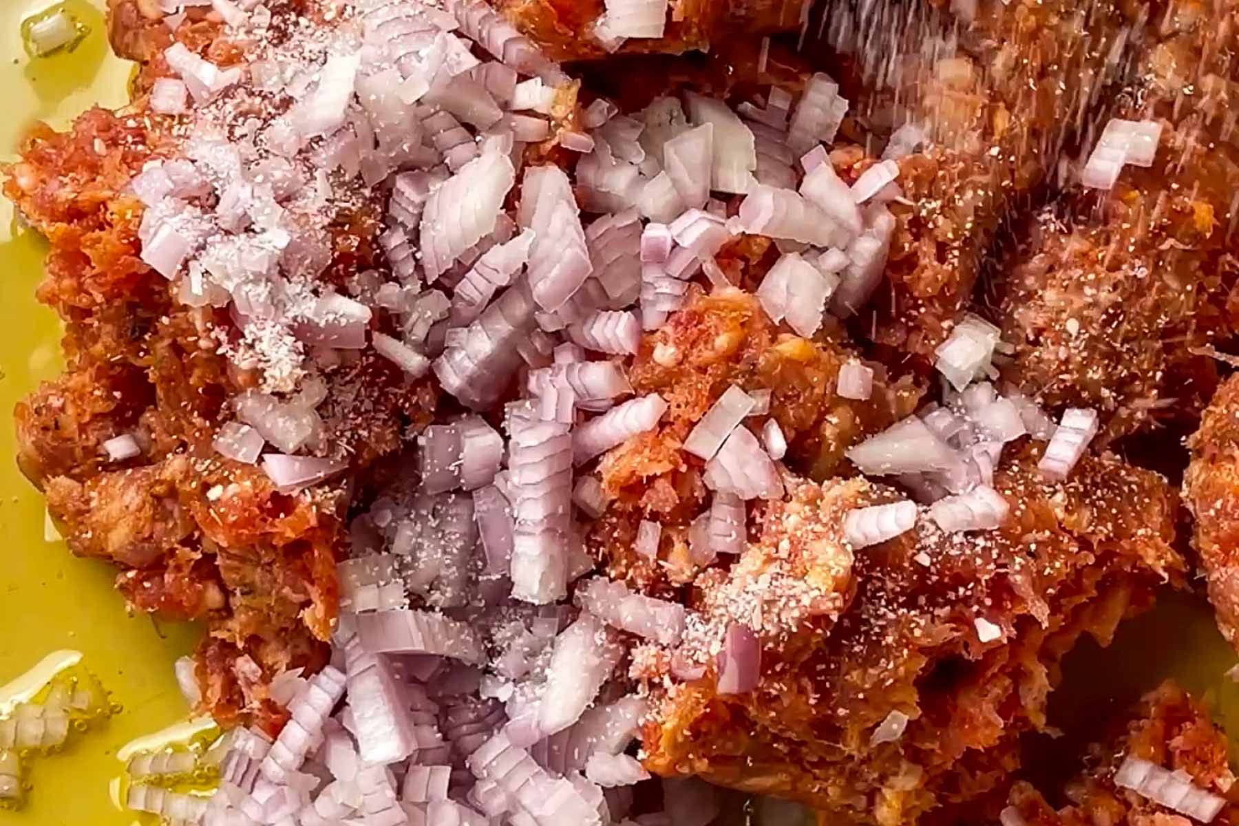 Finely chopped onions and salt sprinkled over a mixture of seasoned minced meat, likely being prepared for a recipe or dish.