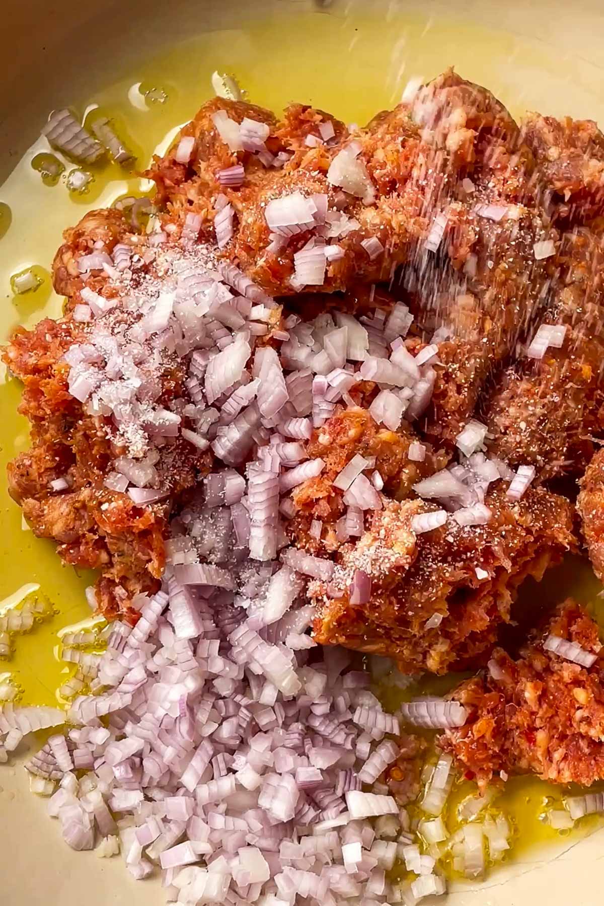 Ground meat, chopped raw shallots, salt, and olive oil are combined in a pan, ready to be mixed and cooked.
