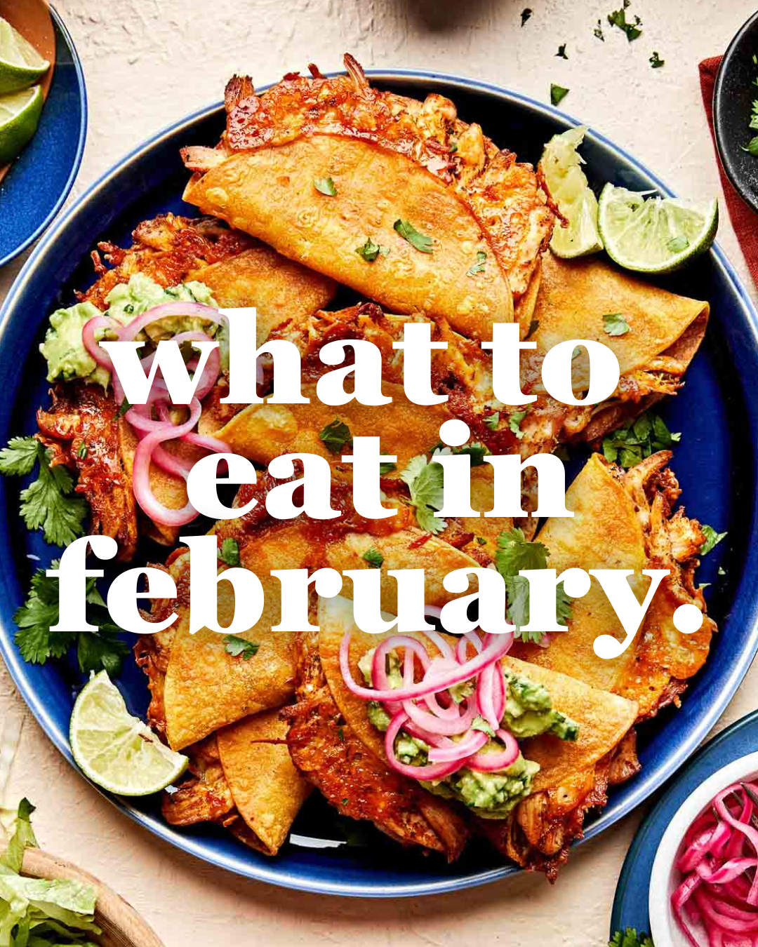 A plate of golden, crispy tacos topped with pickled onions, guacamole, cilantro, and lime wedges, with white text overlay reading “what to eat in february.”.
