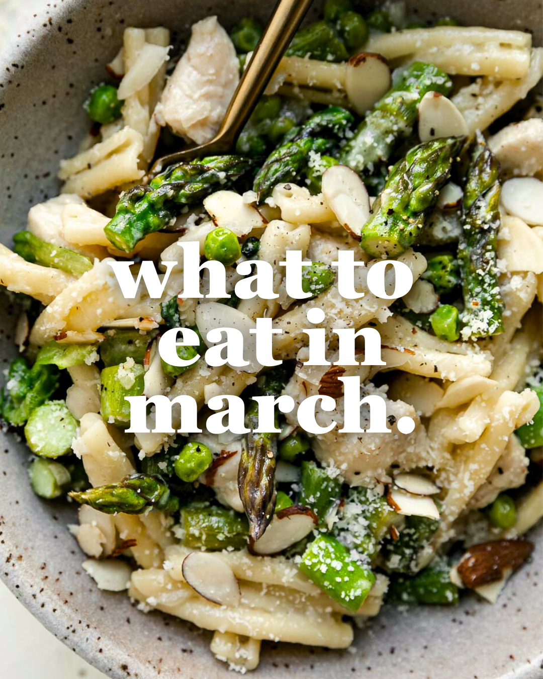 A bowl of pasta with asparagus, peas, sliced almonds, and grated cheese is shown with a gold fork. White text over the image reads, “what to eat in march.”.