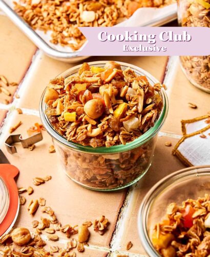 A glass jar filled with homemade granola sits on a tiled surface, surrounded by more granola and jars. A banner reading “Cooking Club Exclusive” is overlaid on the image.