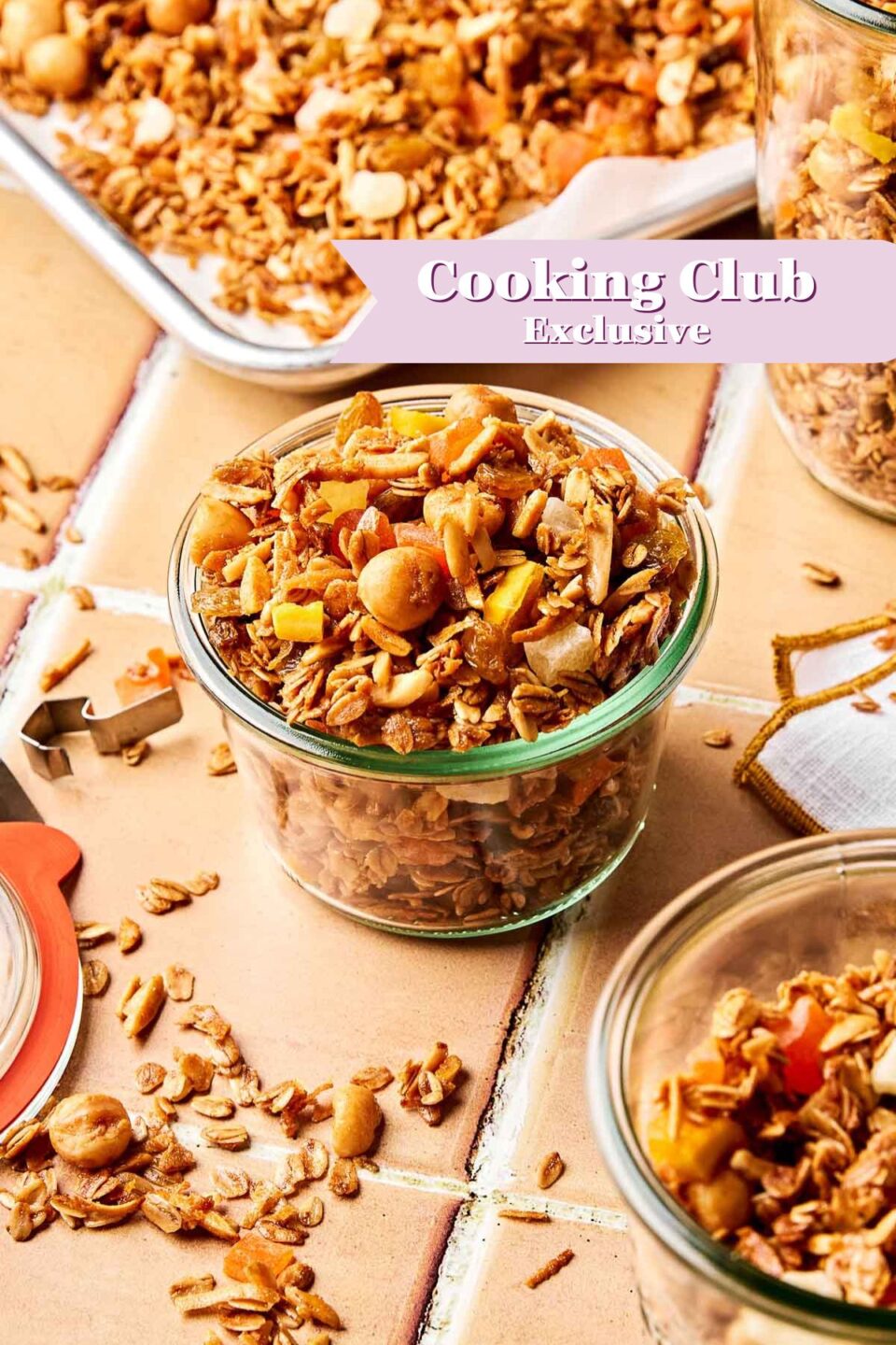 A glass jar filled with homemade granola sits on a tiled surface, surrounded by more granola and jars. A banner reading “Cooking Club Exclusive” is overlaid on the image.
