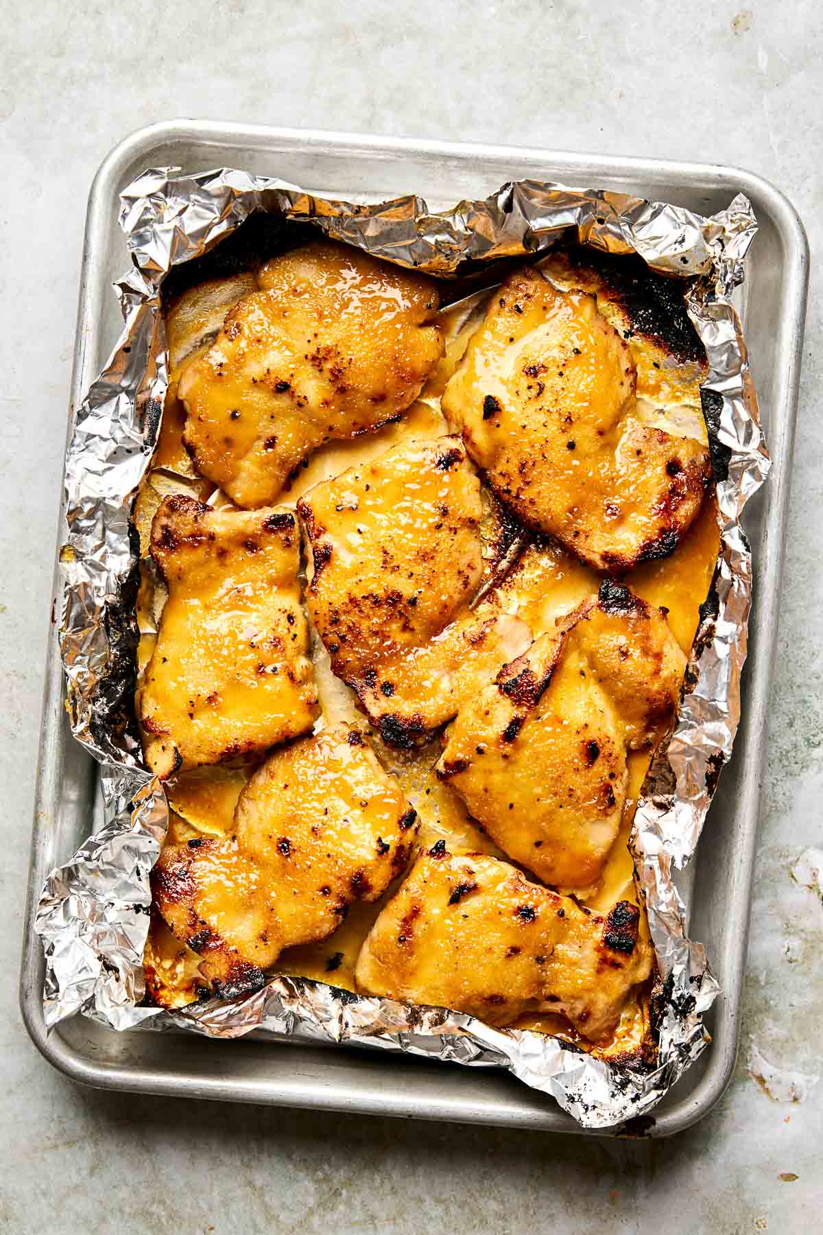 Baked, golden-brown chicken thighs on foil-lined baking sheet, arranged in a single layer with lightly charred edges.