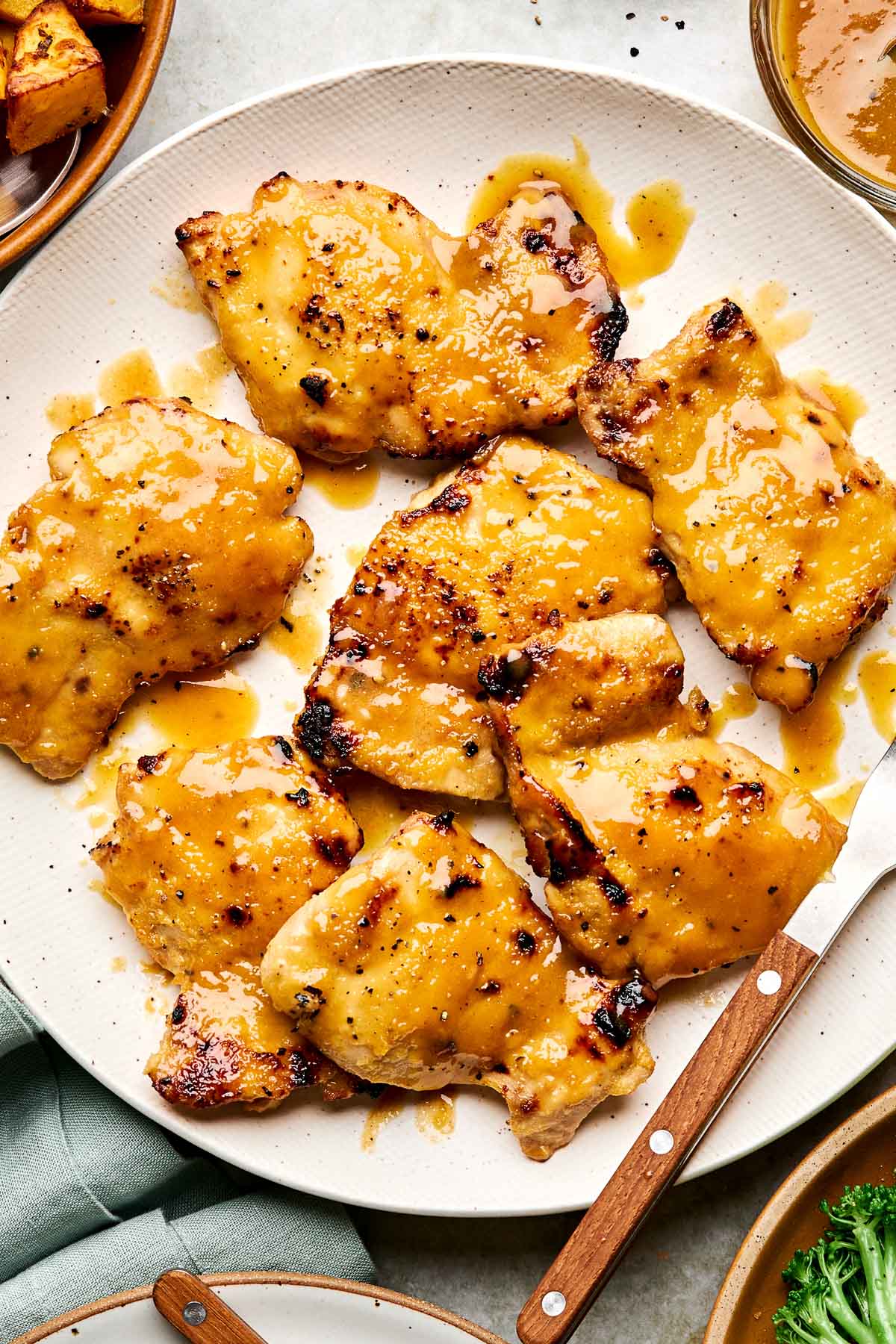 Grilled chicken thighs covered in a glossy honey mustard sauce on a white plate with a wooden-handled knife beside them.