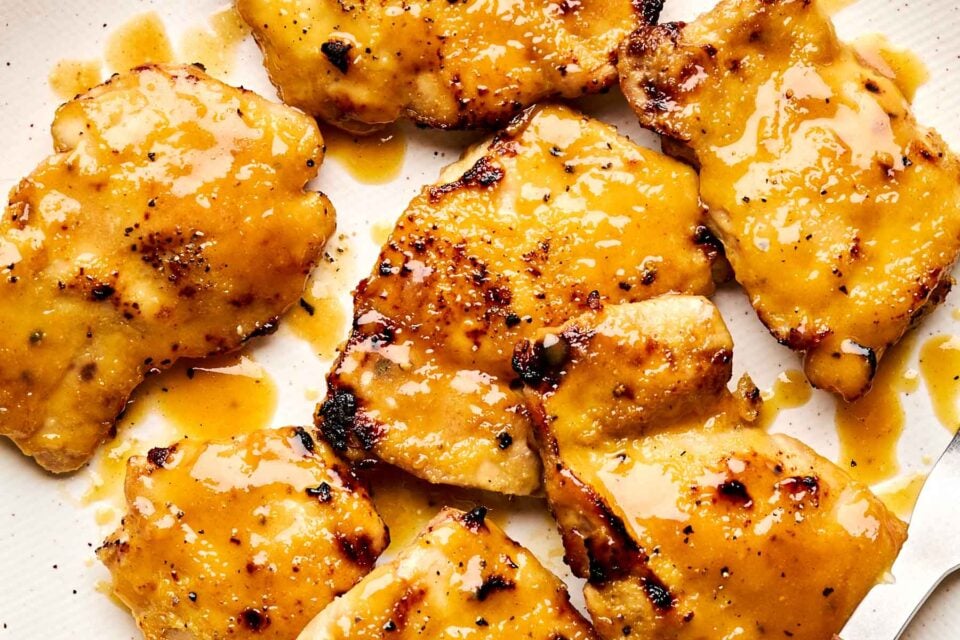 Several pieces of grilled chicken are covered in a glossy golden honey mustard sauce, arranged closely on a white plate.