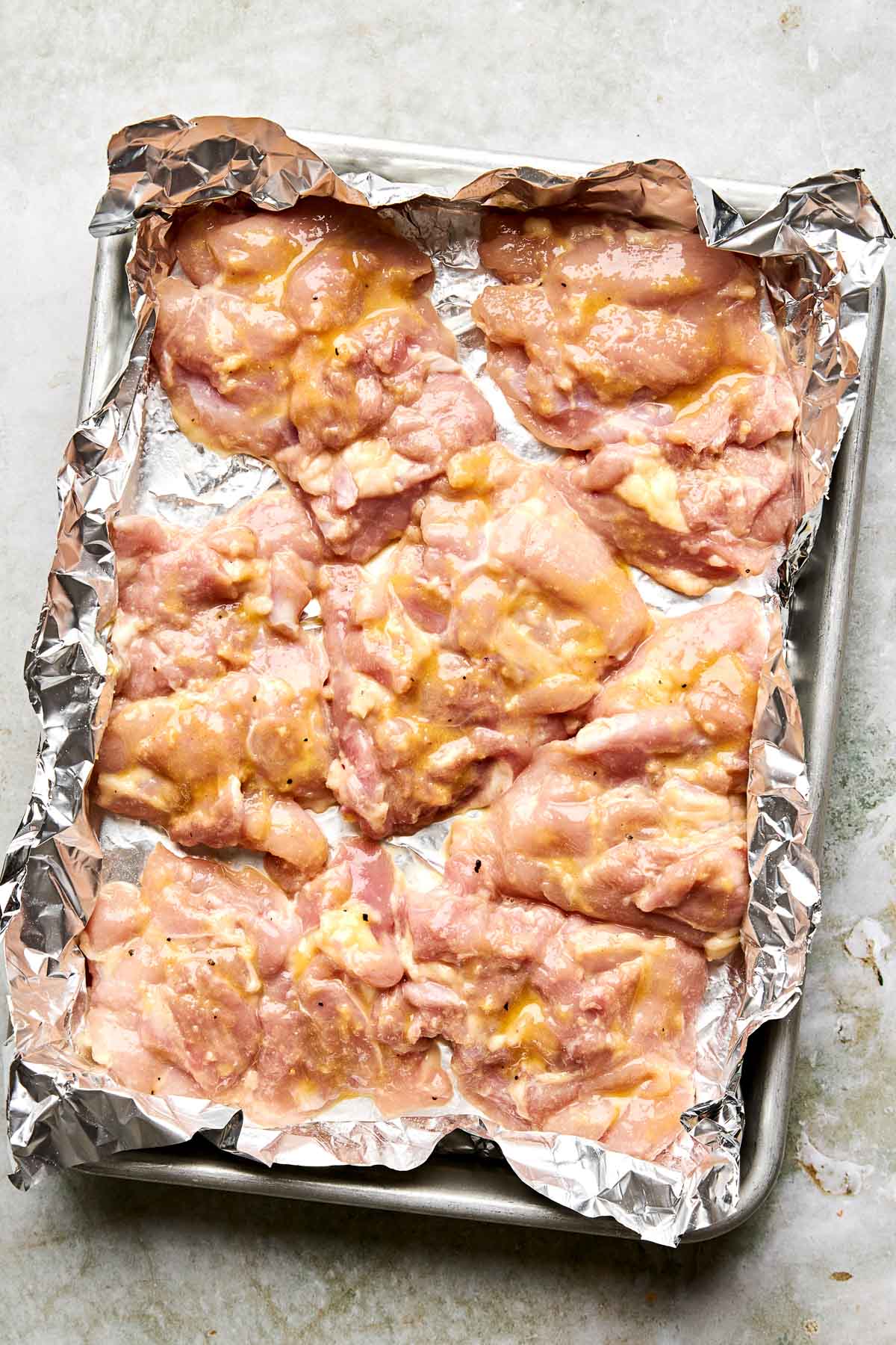 Raw, marinated chicken thighs arranged on a foil-lined baking sheet, ready to be cooked.